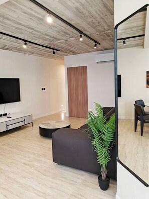 A modern living room with a flat-screen TV, a dark sofa, a round coffee table, and a potted plant. - Ocean Paradise apartment (Mellieħa)