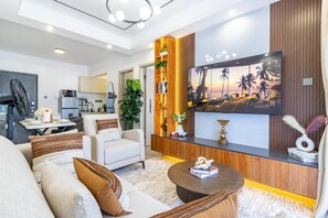 A modern living room with a flat-screen TV, a sofa, a coffee table, and a kitchen in the background. - Cozy 1-bedroom apartment in charming Kilimani Nairobi (Nairobi)
