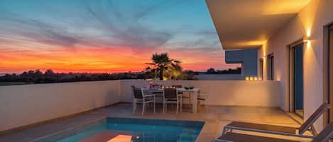 A rooftop pool area with a sunset view, a dining table with chairs, and a small pool.