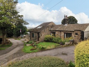 A stone cottage with a garden, a flag, and a paved driveway. - Brownhill Bungalow (Keighley)