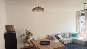 Um espaço de estar moderno com uma mesa de jantar de madeira, cadeiras de vime, um sofá e uma janela grande.