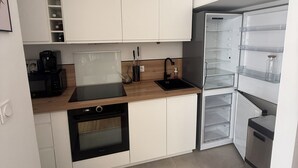 Cozinha compacta com armários brancos, bancada preta, forno embutido, pia e geladeira.