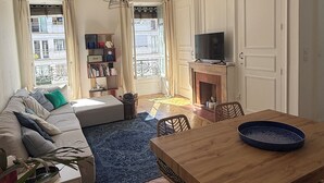 Uma sala de estar com sofá, mesa de jantar, televisão e lareira.