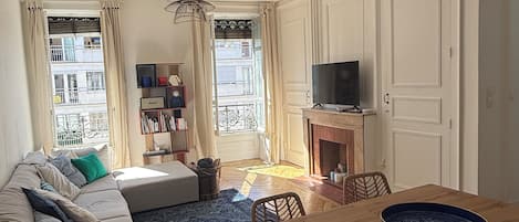 A living room with a sofa, a dining table, a television, and a fireplace.
