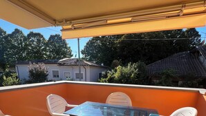 Eine Terrasse im Freien mit einem Glastisch und weißen Plastikstühlen, umgeben von orangefarbenen Wänden und einem gefliesten Boden.