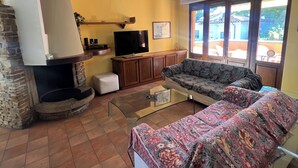 Ein Wohnzimmer mit Kamin aus Stein, einer Couch, einem Fernseher und einem Balkon mit Blick.