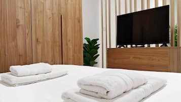 Un dormitorio moderno con un armario de madera, un televisor de pantalla plana grande y toallas blancas ordenadas sobre la cama.