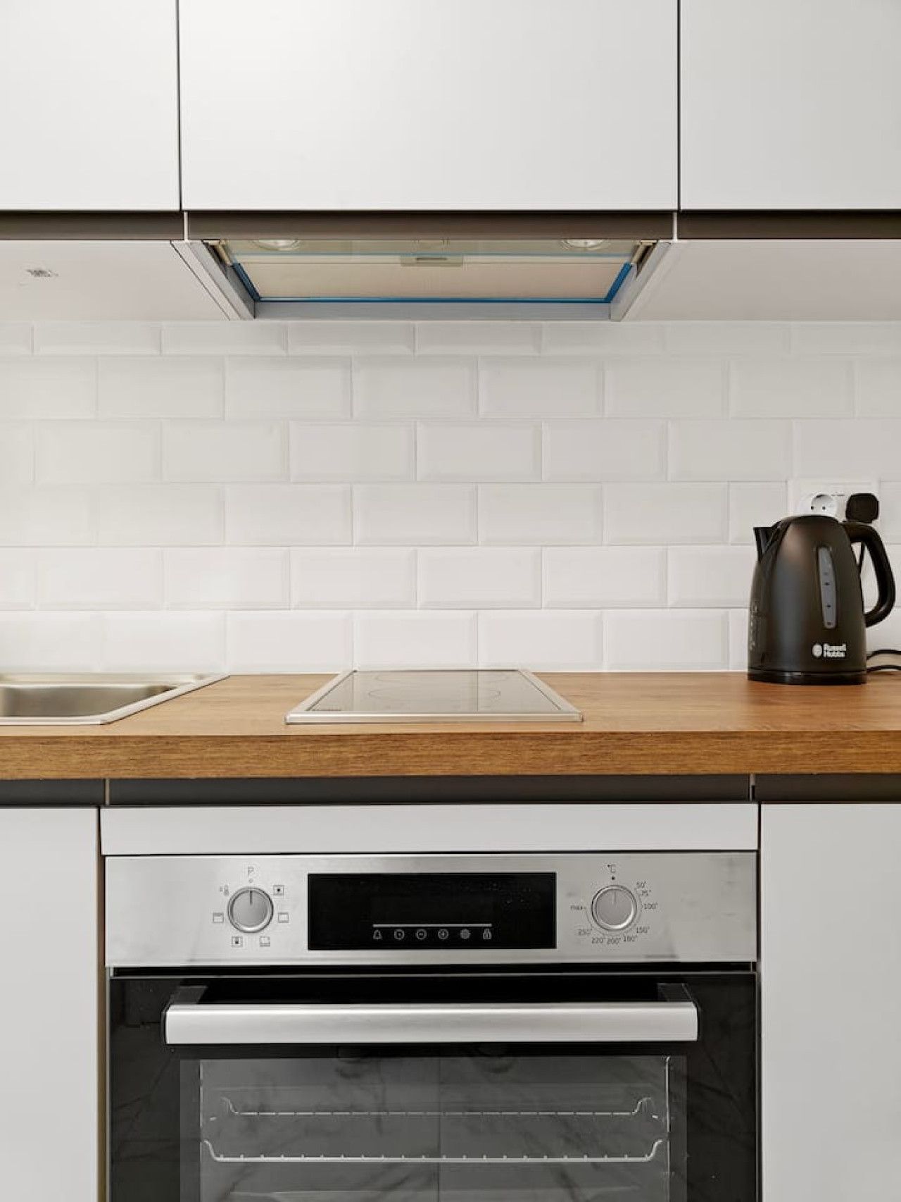 Una cocina con horno empotrado, hervidor y campana extractora de acero inoxidable.