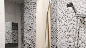 Un baño con ducha, lavamanos y espejo.
