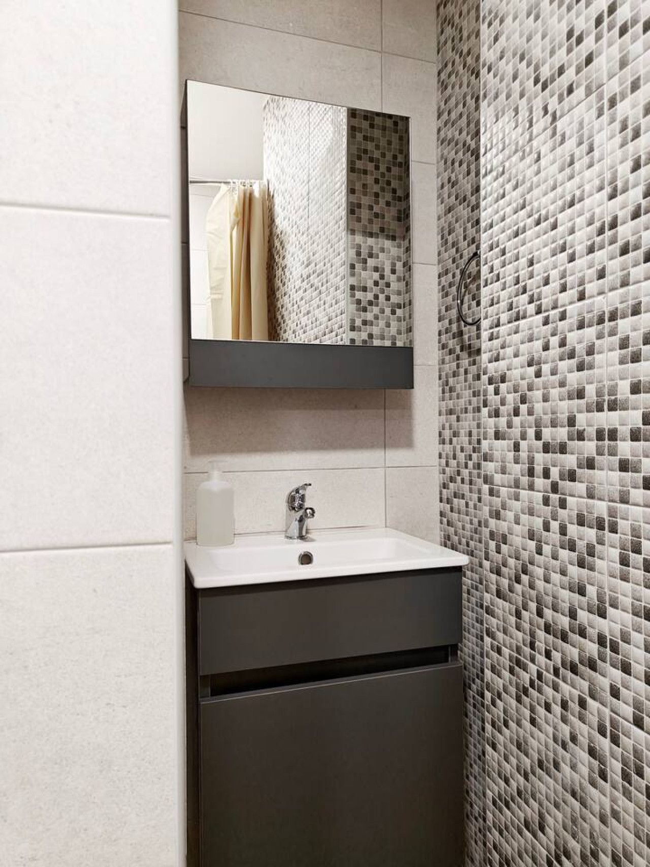 Une salle de bain avec un lavabo blanc, un miroir au-dessus et un mur recouvert de carreaux formant une mosaïque.