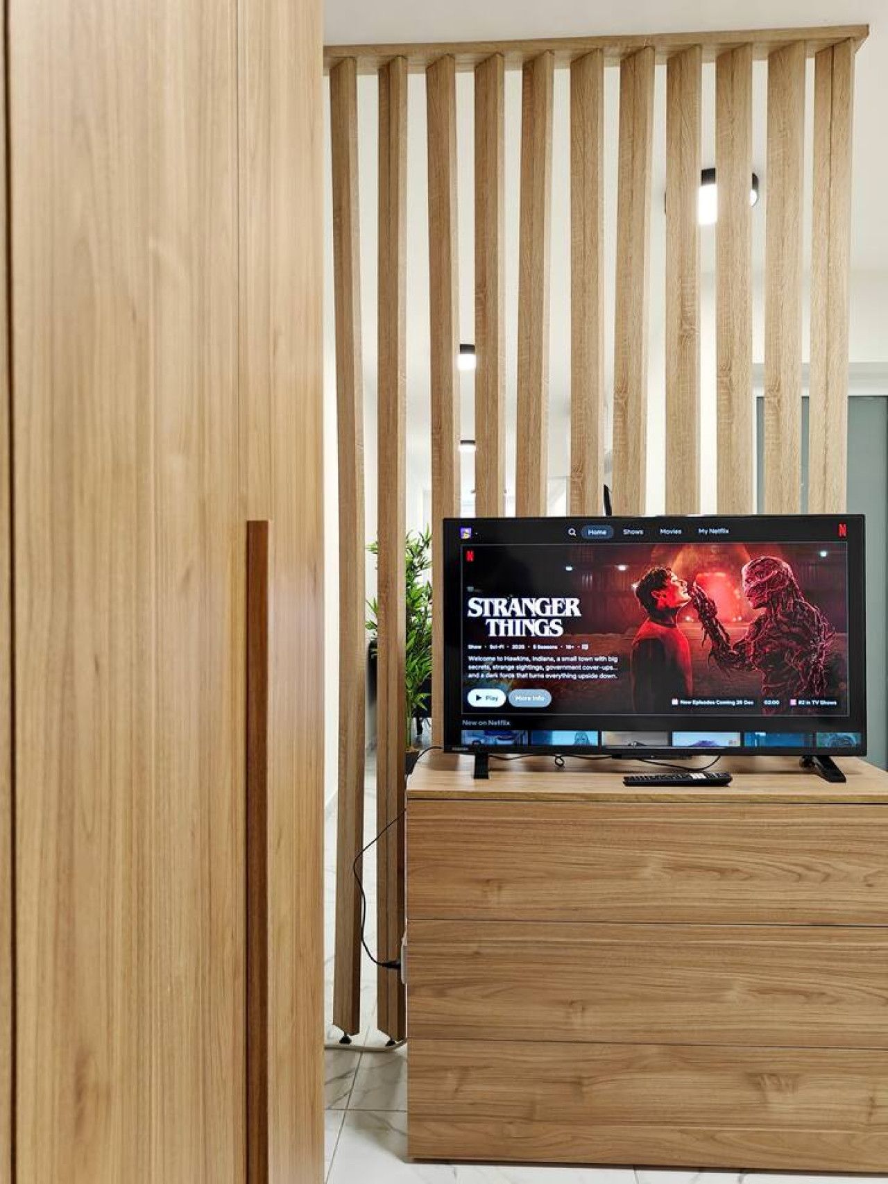 Un téléviseur à écran plat, posé sur un meuble en bois, affiche l’interface Netflix et la série « Stranger Things ».