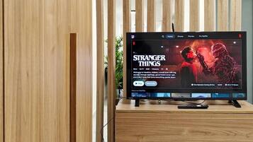 Un téléviseur à écran plat, posé sur un meuble en bois, affiche l’interface Netflix et la série « Stranger Things ».