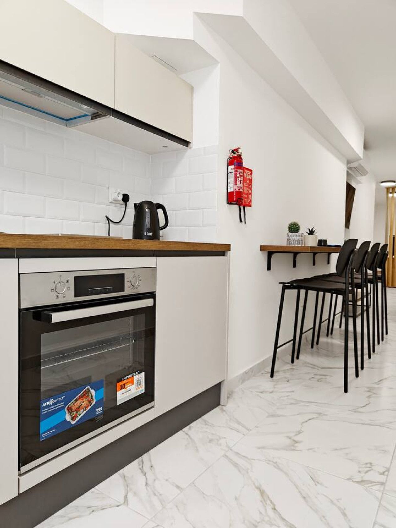 Una cocina moderna con horno empotrado, hervidor y extintor de incendios en la pared.