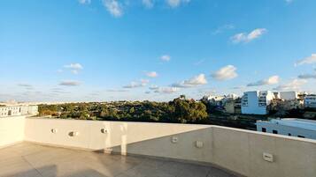 A rooftop terrace with a clear view of a cityscape, including buildings and trees.