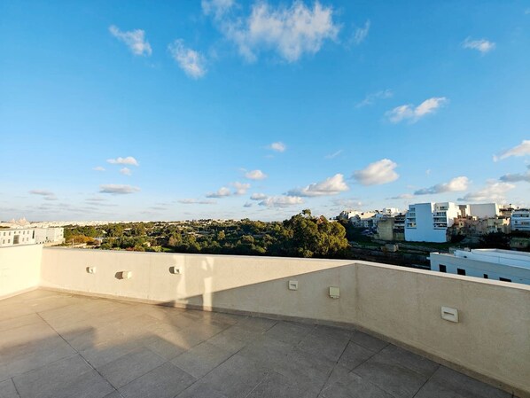 A rooftop terrace with a clear view of a cityscape, including buildings and trees.