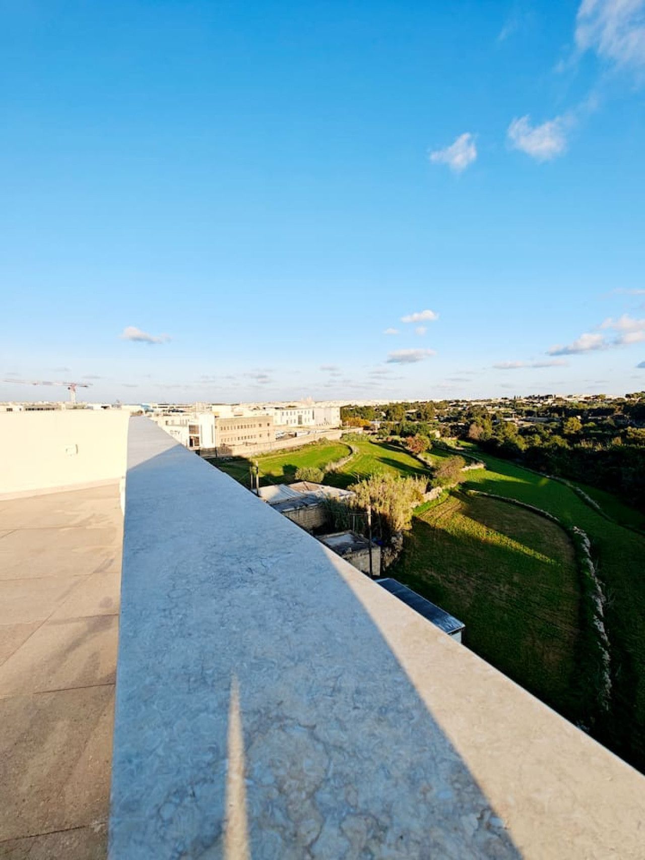 Una terraza en la azotea con vistas despejadas a un paisaje urbano, que incluye un edificio grande y zonas verdes circundantes.