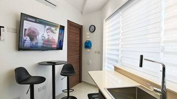 A modern kitchen with a built-in sink, a flat-screen TV mounted on the wall, and two black bar stools.