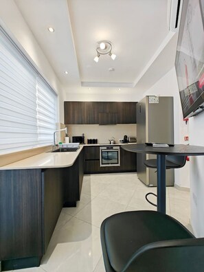 A modern kitchen with dark wood cabinets, a built-in oven, and a small dining table with a chair.