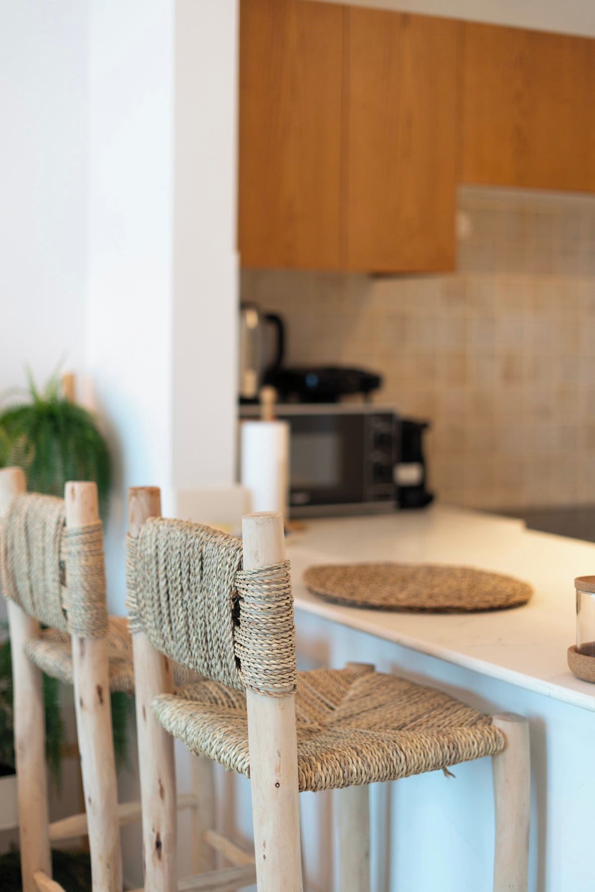 Une cuisine avec un plan de travail blanc, des chaises en bois avec des assises en osier, et une cuisinière bien visible.