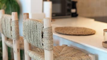 Une cuisine avec un plan de travail blanc, des chaises en bois avec des assises en osier, et une cuisinière bien visible.
