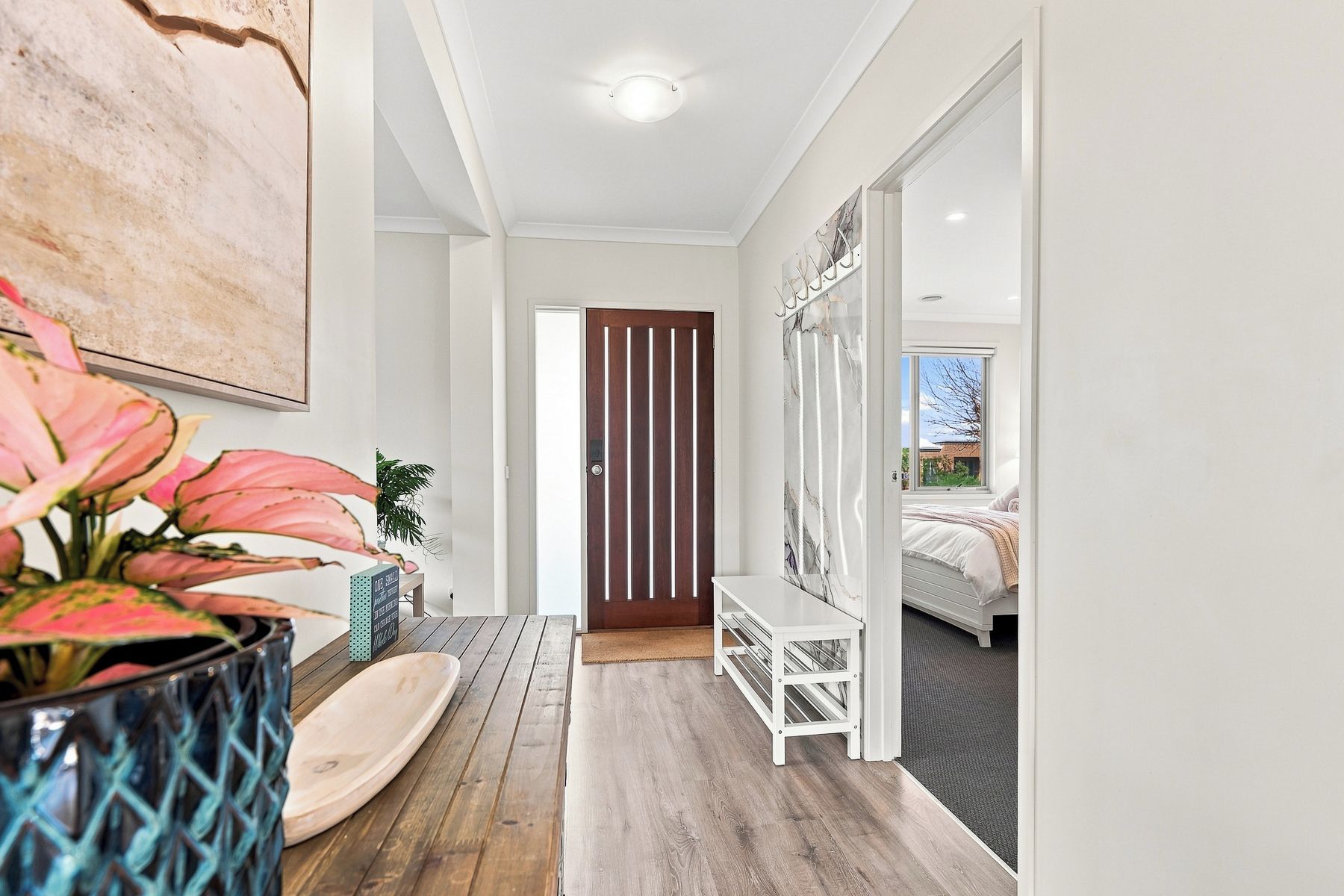 Un couloir avec un plancher en bois, une porte blanche, un banc blanc et un lit à l’arrière-plan.