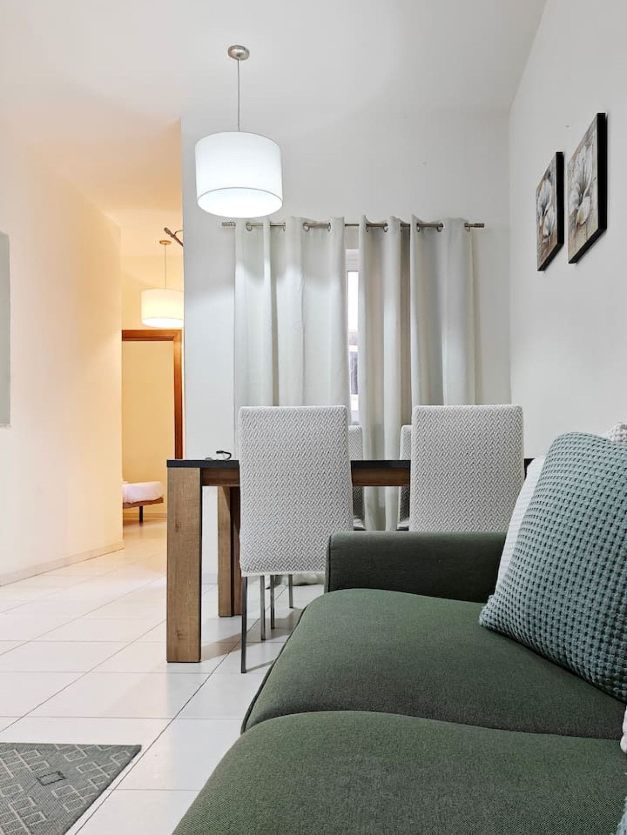 A modern living room with a green sofa, two chairs, a wooden side table, and a hanging light fixture.
