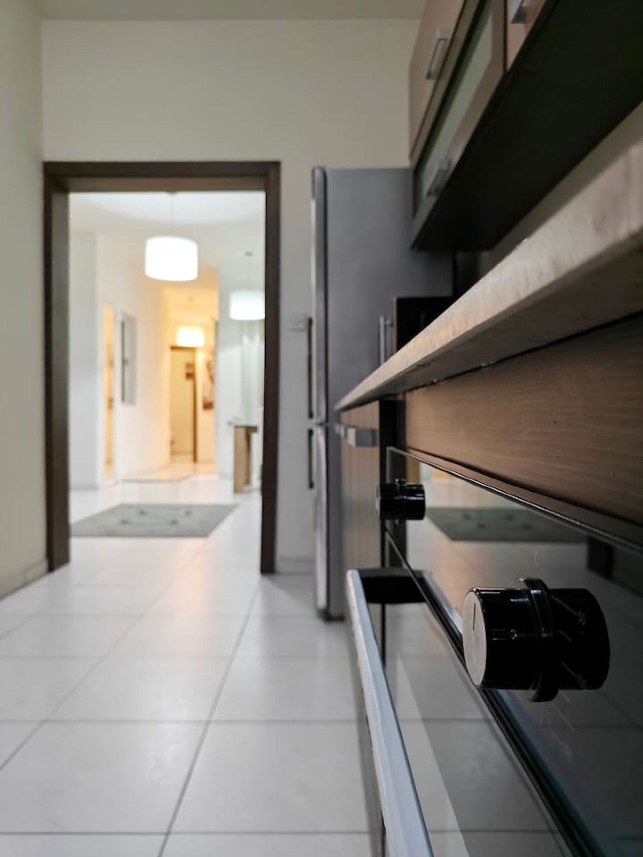 Ein Flur mit einem Kühlschrank und einer Mikrowelle auf einer Arbeitsplatte, der zu einem Raum mit einer Tür und einer Leuchte führt.