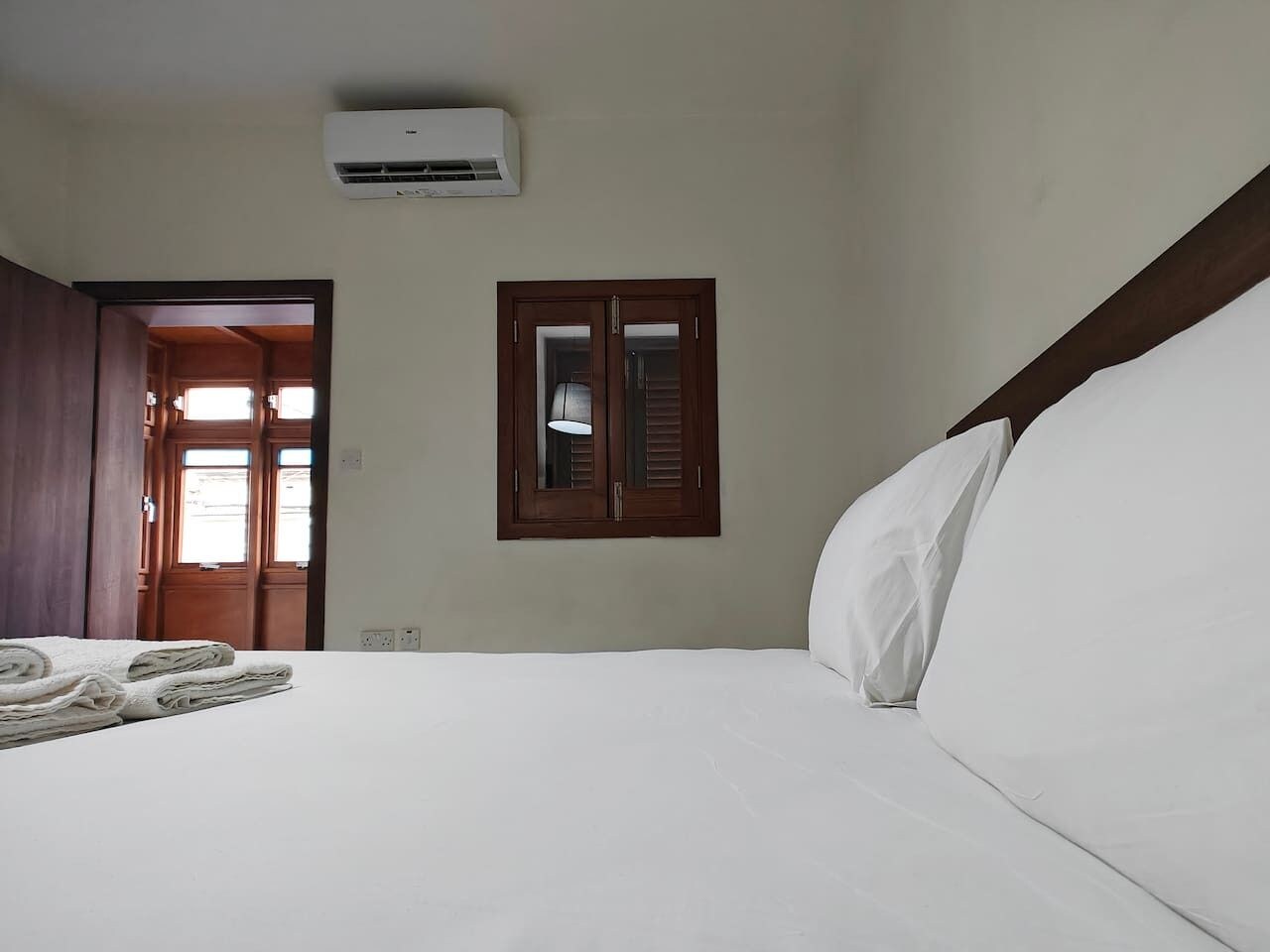 Ein Hotelzimmer mit Bett, Klimaanlage, einem Fenster mit Rollläden und einer Tür zu einem anderen Raum.