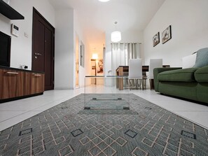 Ein modernes Wohnzimmer mit einem Glastisch, einem grünen Sofa und einem gemusterten Teppich.