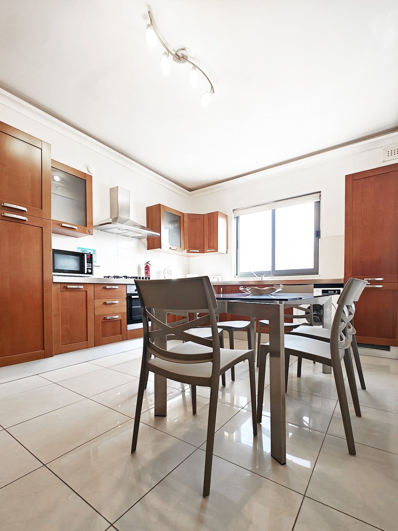 A modern kitchen with wooden cabinets, a microwave, and a dining area with chairs.