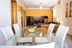 A dining area with a glass table, white chairs, a laptop, and a banana bowl.