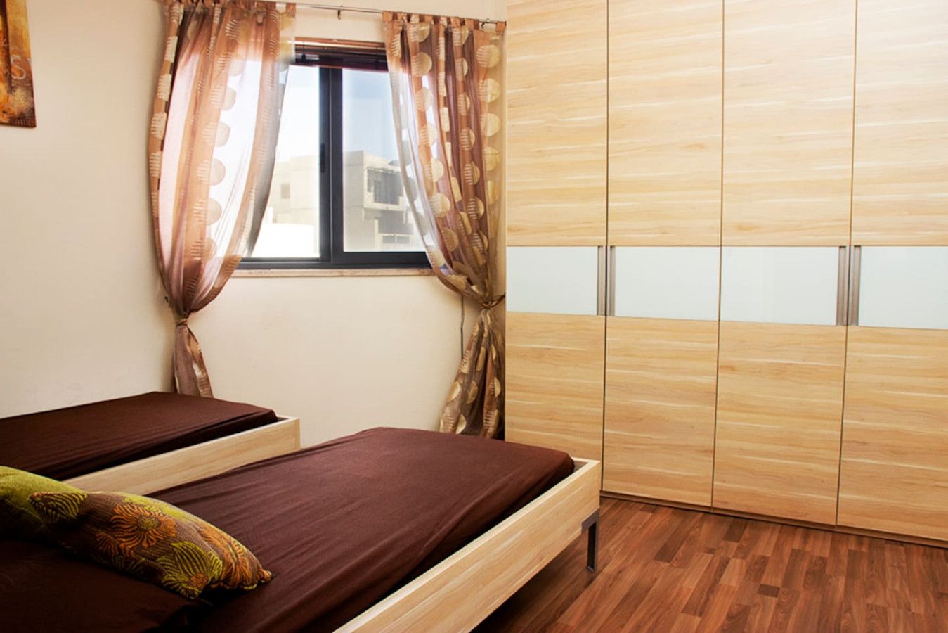 A bedroom with two beds, a window with curtains, and a wardrobe.