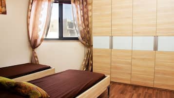 A bedroom with two beds, a window with curtains, and a wardrobe.