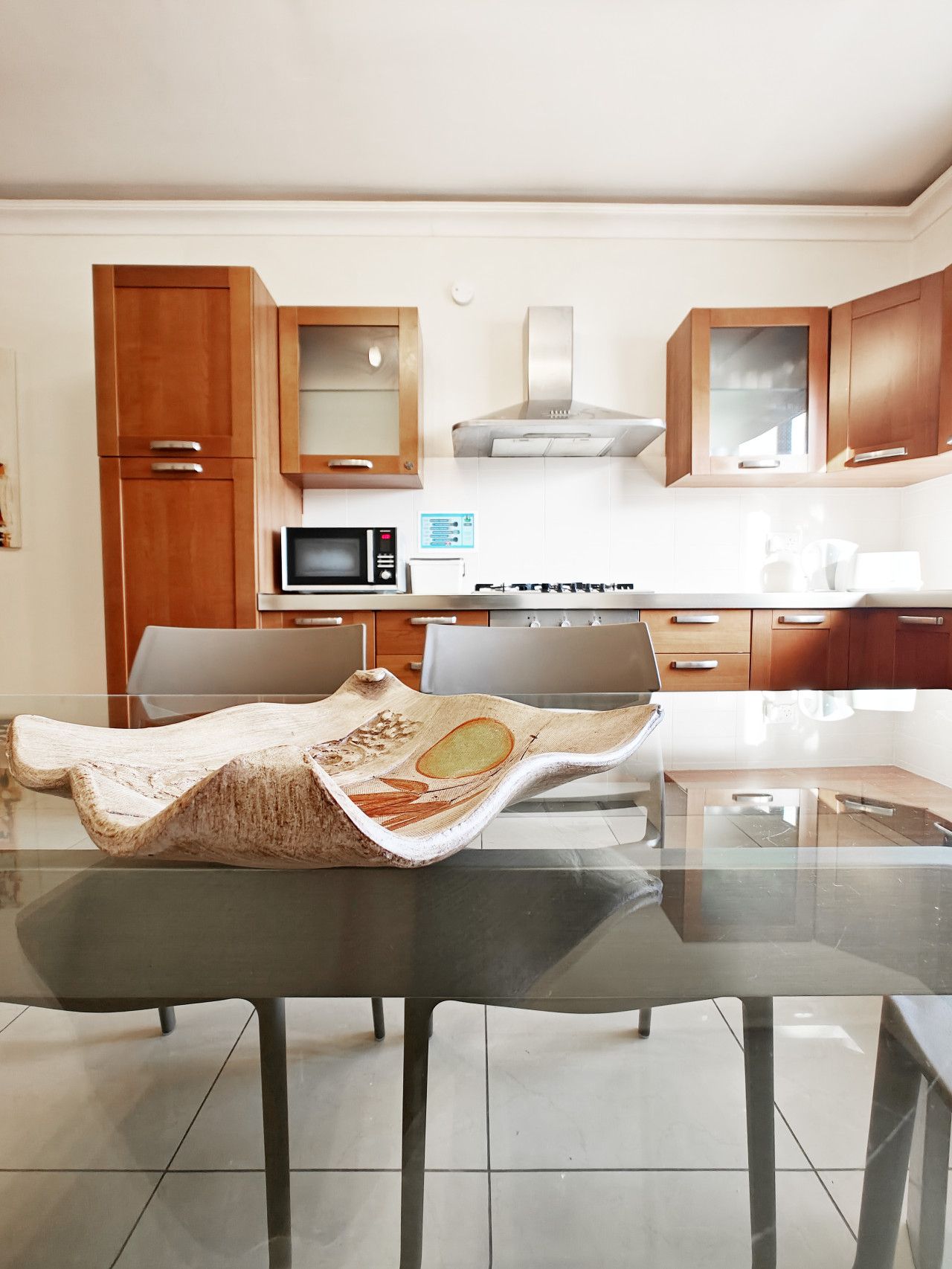 A modern kitchen with wooden cabinets, a microwave, a stove, and a glass dining table.