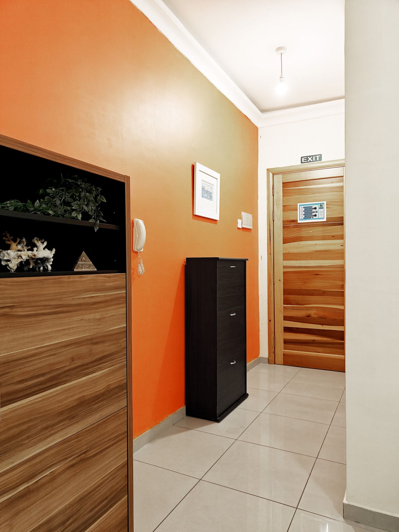 A hallway with an orange wall, a black cabinet, a framed picture, and an exit door.