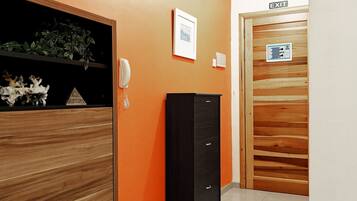 A hallway with an orange wall, a black cabinet, a framed picture, and an exit door.