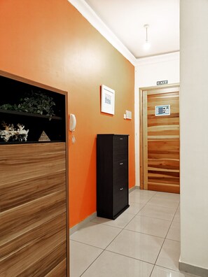 A hallway with an orange wall, a black cabinet, a framed picture, and an exit door.