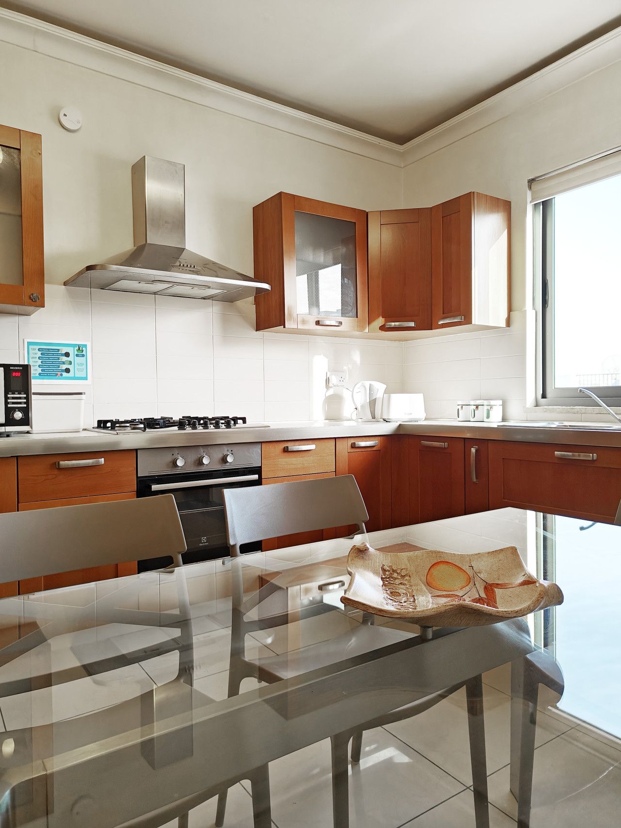 A modern kitchen with wooden cabinets, stainless steel appliances, and a glass dining table.