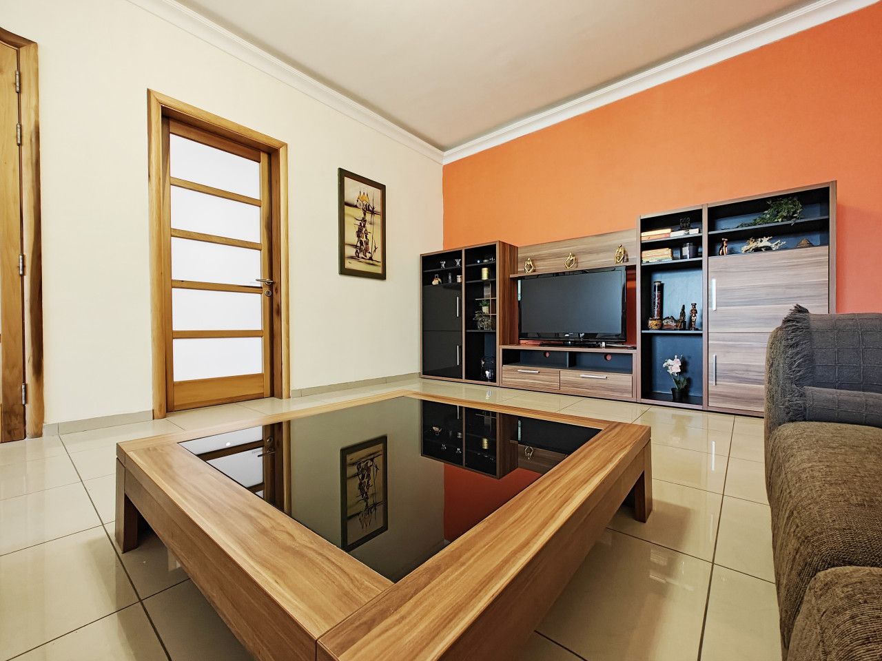 A living room with a glass-top coffee table, a sofa, a TV, and built-in shelving.