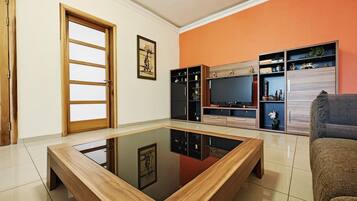 A living room with a glass-top coffee table, a sofa, a TV, and built-in shelving.
