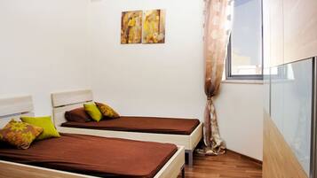 A room with two beds, a window with curtains, and two wall-mounted paintings.