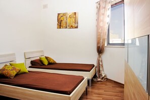 A room with two beds, a window with curtains, and two wall-mounted paintings.