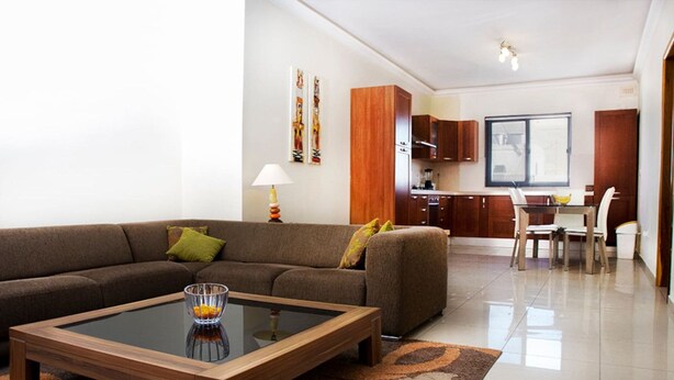 A modern living room with a sofa, coffee table, and a dining area with chairs and a table. - Ivy 2 bedroom apartment (Swieqi)