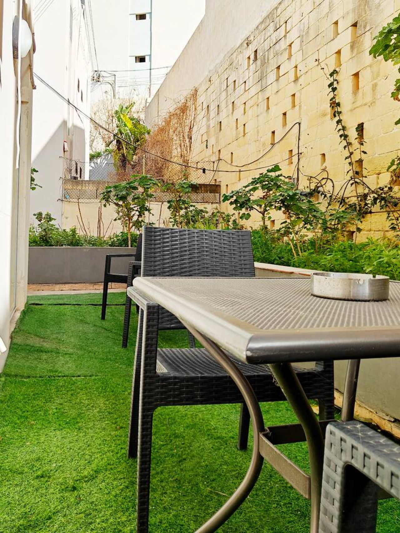 A patio with a table and chairs, surrounded by a small patch of artificial grass and some plants.