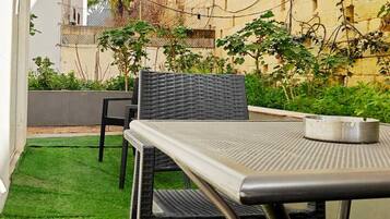A patio with a table and chairs, surrounded by a small patch of artificial grass and some plants.