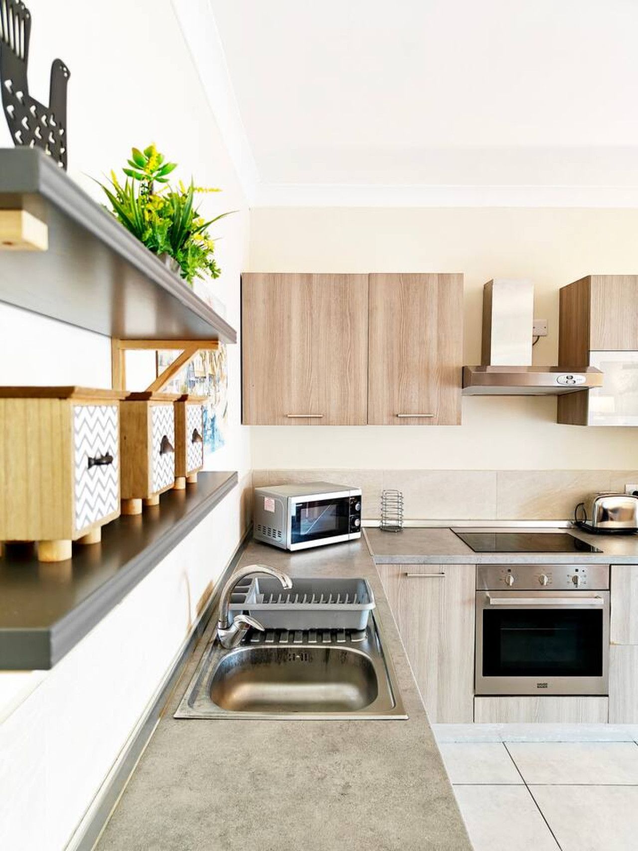 A modern kitchen with wooden cabinets, a stainless steel sink, a microwave, a toaster, and a built-in oven.