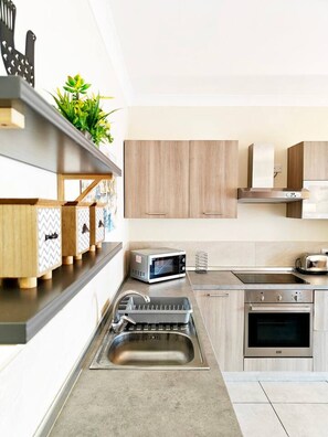 Una cocina moderna con armarios de madera, un lavamanos de acero inoxidable, un microondas, un tostador y un horno empotrado.