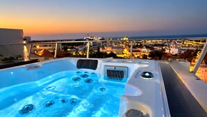 Een bubbelbad met straalmassages, omringd door een balkon met uitzicht op een stadsbeeld bij zonsondergang.