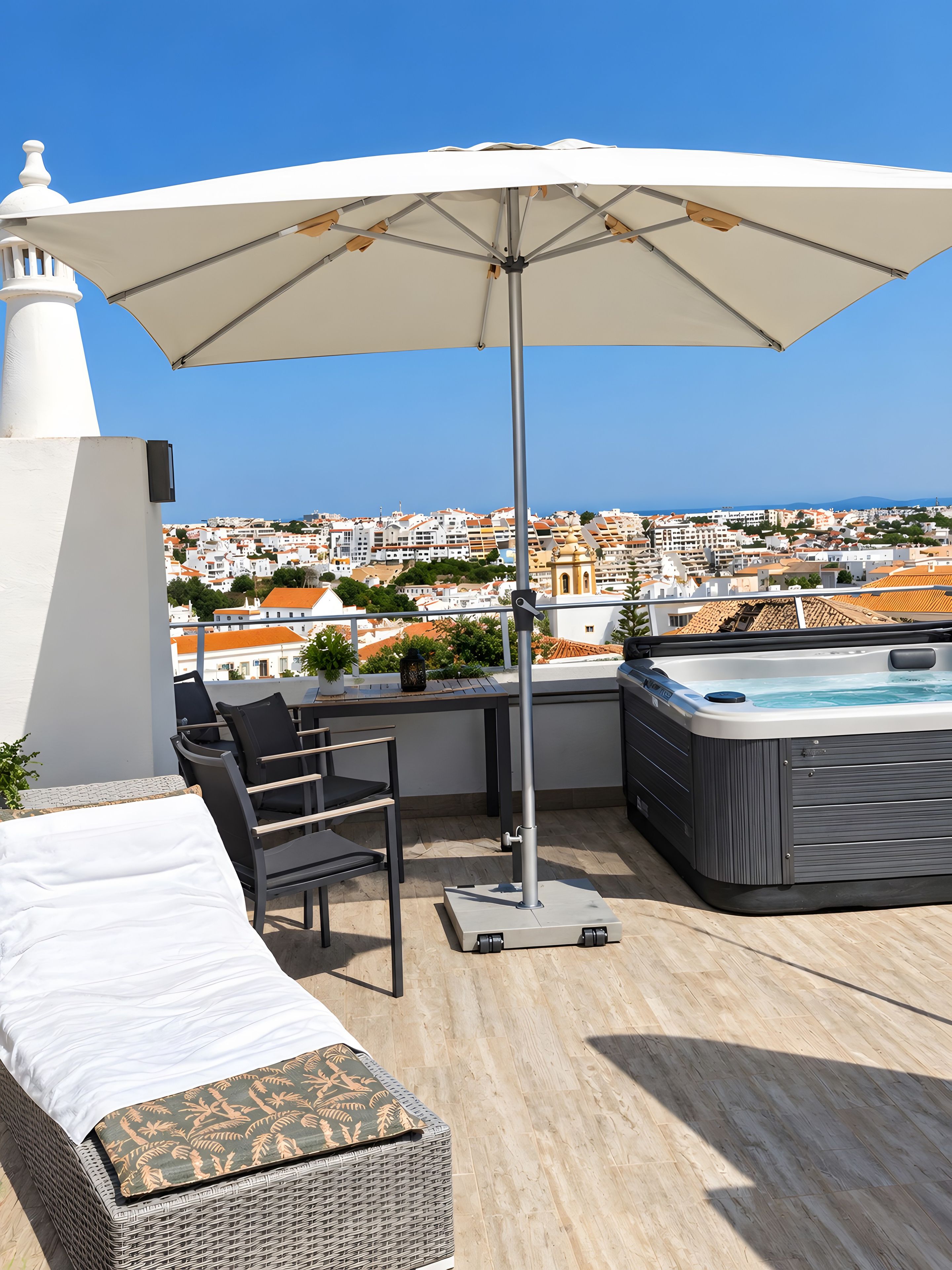 A rooftop terrace with a hot tub, lounge chairs, and an umbrella.