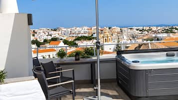 A rooftop terrace with a hot tub, lounge chairs, and an umbrella.